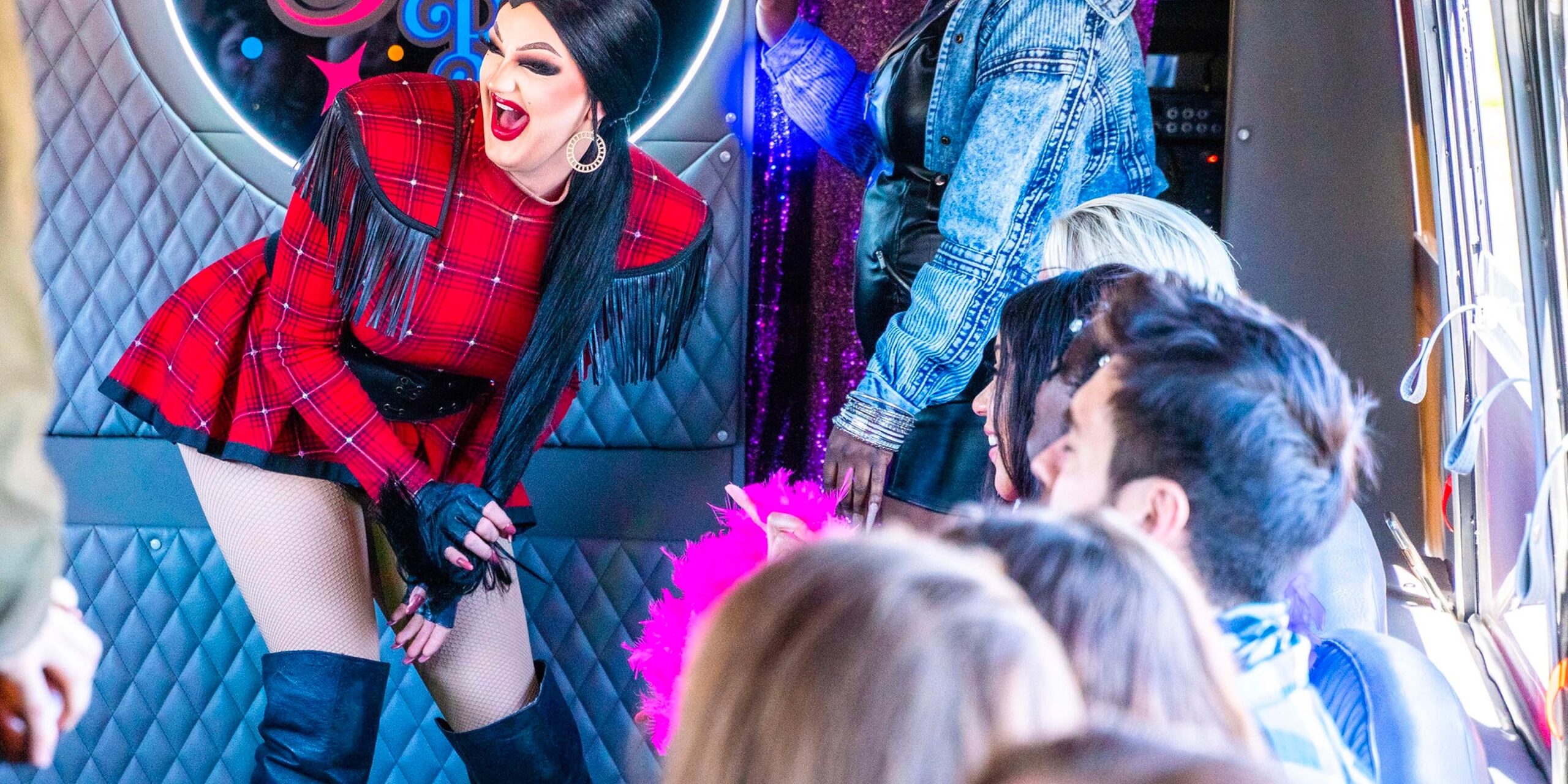 a drag queen in a red and black outfit laughs during her performance on the big drag bus