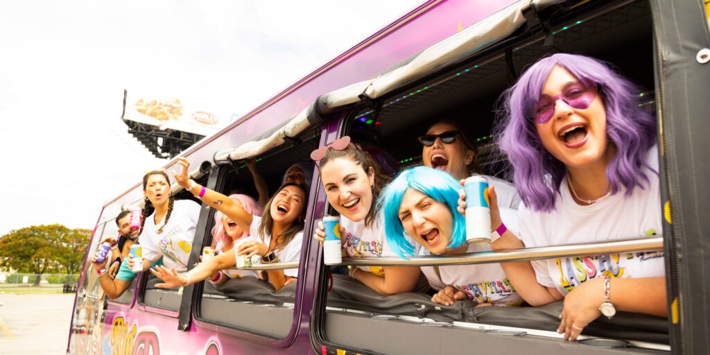 women in wigs and bachelorette party tshirts laughing during a big drag bus tour