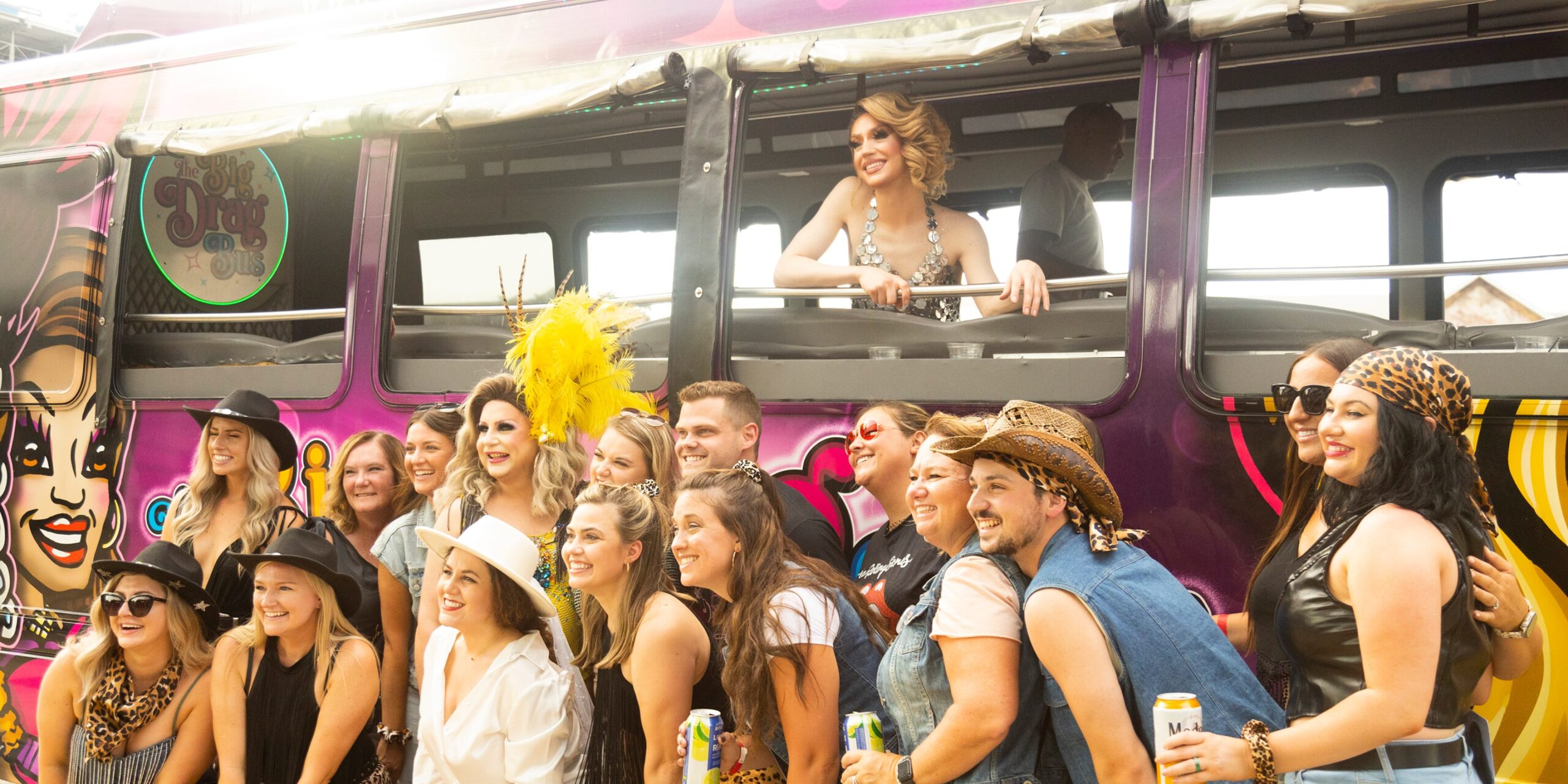 a bachelorette party smiles with drag queens standing outside of the big drag bus