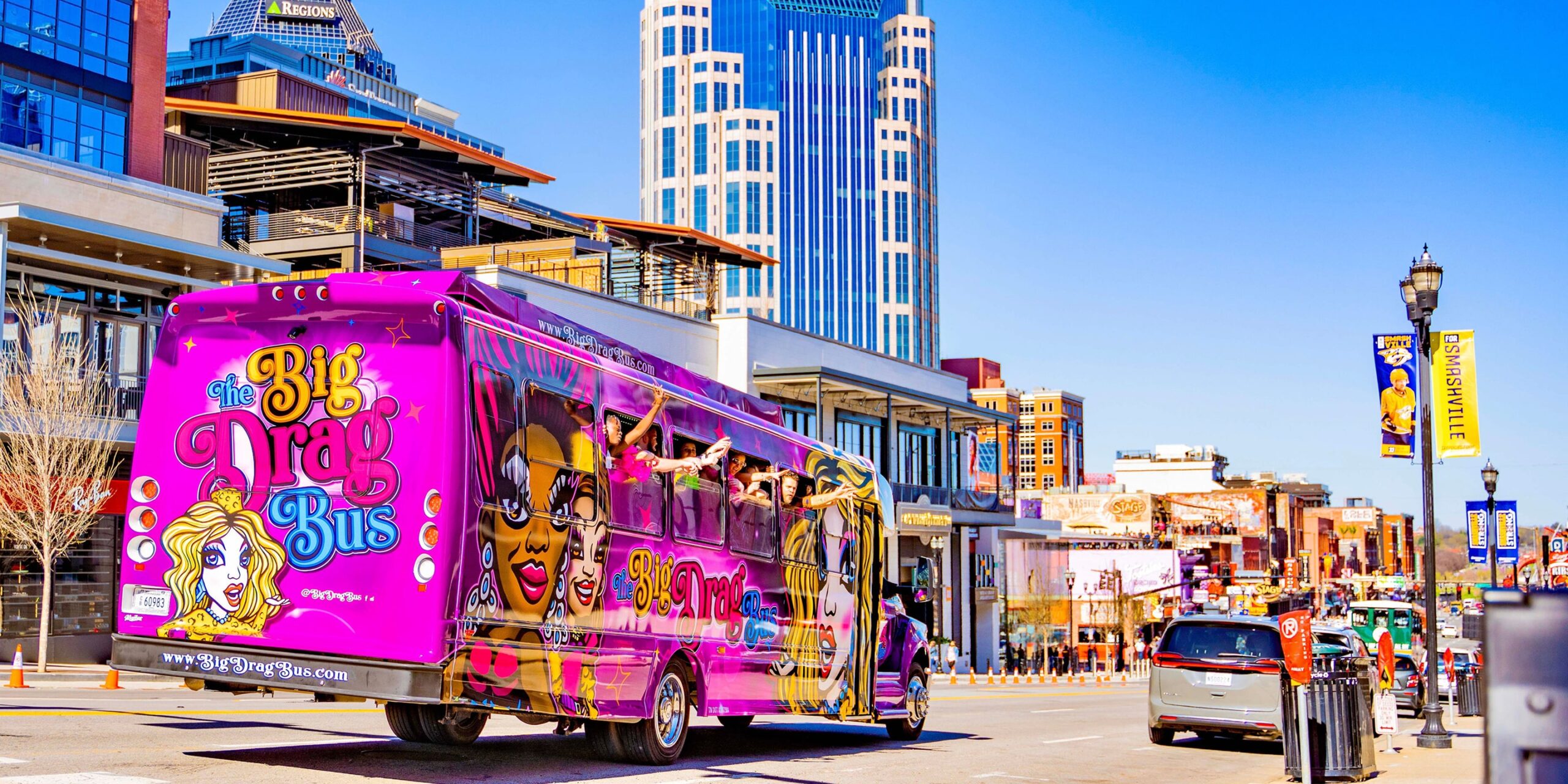 the hot pink nashville drag bus party bus drives down a street in nashville